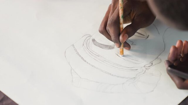 Black illustrator refining hat sketch on paper, closeup of black hands using thin brush for dotted lines with phone reference at side, bright natural light, precise rhythm and steady patience