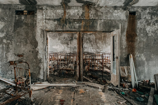 View of abandoned rusty metal bed frames in a decaying room with peeling paint and debris in Pripyat, Kyiv Oblast, Ukraine.
