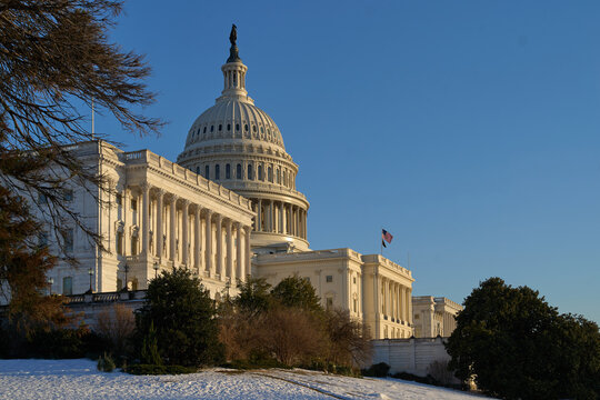 Last beams of golden sunlight on the United States Capitol Building in Washington, DC, with the American flag waving, blue sky backrgound