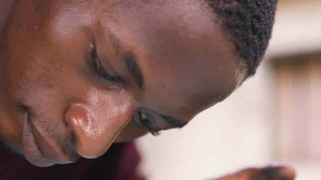 Tight closeup black man inspecting detail, beads of sweat on brow, neutral background, concentrated profile, careful precision and silent intensity in smallscale craft or studio work