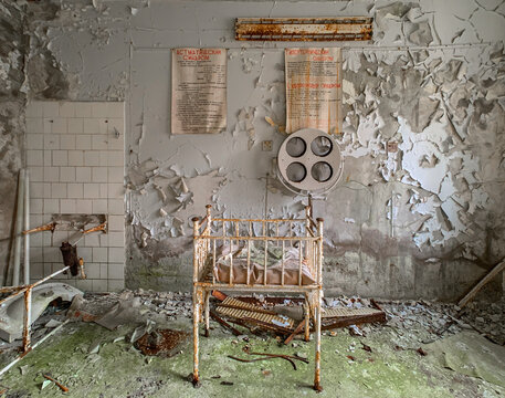 View of an abandoned hospital room with a rusty metal crib, peeling paint on the walls, and old medical equipment in Pripyat, Kyiv Oblast, Ukraine.