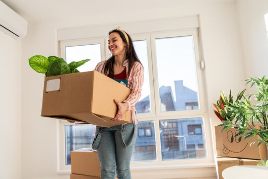 Woman carries a box with a plant while moving into a new apartment during daylight hours