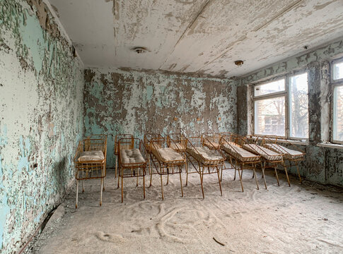 View of an abandoned hospital room with rows of metal baby cribs and peeling paint on the walls in Pryp'yat', Kyiv Oblast, Ukraine.