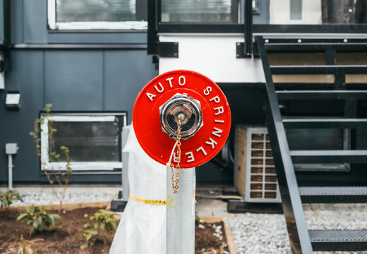 Red auto sprinkler standpipe connector outside building. FDC or Fire department connection for water supply during fire emergency. Exterior access point for firefighting operations. Selective focus.