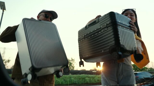  Happy young couple lifting luggage into car near airport. Travel preparation in road trip. Summer vacation and modern travel lifestyle with safe driving concept.
