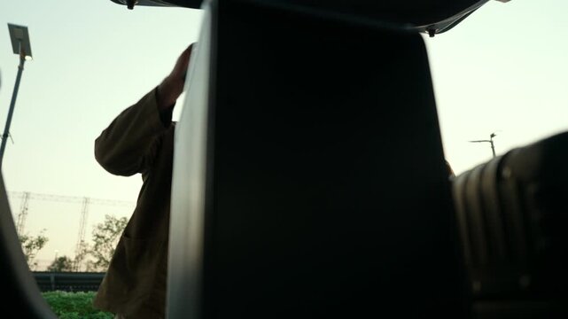  Happy young couple lifting luggage into car near airport. Travel preparation in road trip. Summer vacation and modern travel lifestyle with safe driving concept.
