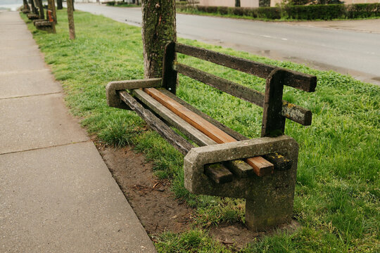 Old wooden bench placed near empty wet street and green grass. It reflects solitude, quiet urban life and contemplative mood.