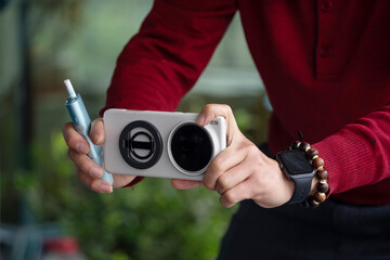 Fototapeta premium A man in red shirt holds a white dual-camera smartphone and a blue stylus pen