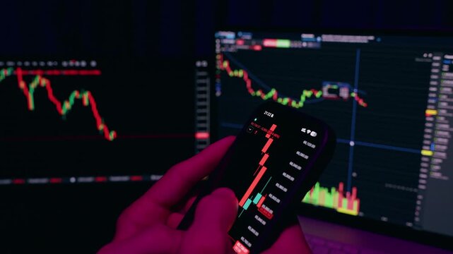 Hand Using Smartphone With Cryptocurrency Chart While Laptop Shows Market Data In Background In Time Lapse Effect With Red And Blue Lighting Representing Active Trading And Analysis Concept
