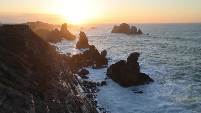 View of the dramatic Urros de Liencres rock formations and sea stacks with waves crashing against the cliffs during a golden sunset in Liencres, Cantabria, Spain.