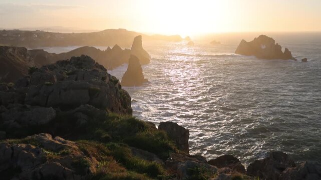 View of the Urros de Liencres sea stacks and rugged cliffs under a golden sunset light in Liencres, Cantabria, Spain.