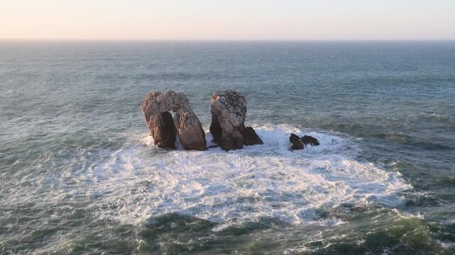 View of Urros de Liencres rock formations with waves crashing against the stone under a soft sunset sky Liencres, Cantabria, Spain.