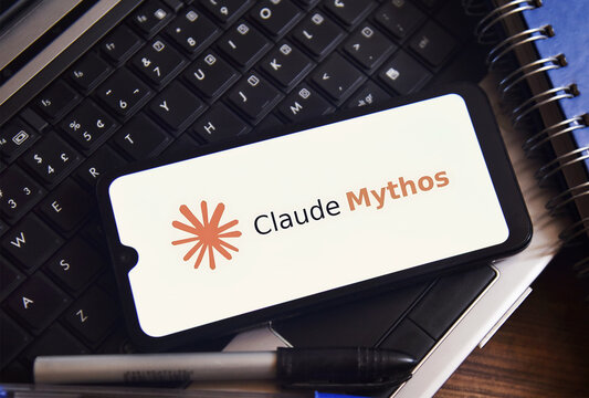 The Claude Mythos logo is displayed on a smartphone screen on a table with office objects. Concept of technology, computing, and innovation.