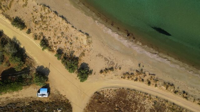 High-angle aerial view of the Neftina Beach on Limnos Island, Greece, showing crystal clear turquoise waters meeting a sandy shoreline backed by rugged, arid Mediterranean hills.