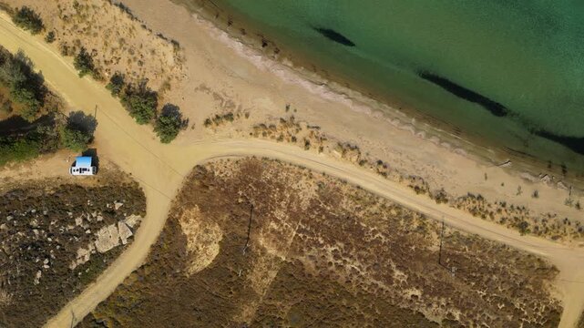 High-angle aerial view of the Neftina Beach on Limnos Island, Greece, showing crystal clear turquoise waters meeting a sandy shoreline backed by rugged, arid Mediterranean hills.