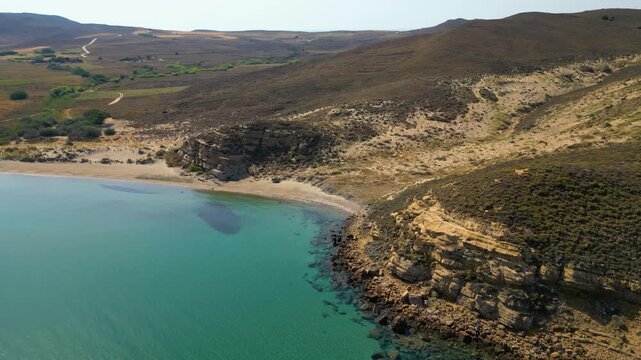 High-angle aerial view of the Neftina Beach on Limnos Island, Greece, showing crystal clear turquoise waters meeting a sandy shoreline backed by rugged, arid Mediterranean hills.