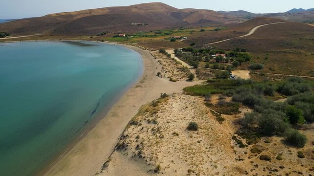 High-angle aerial view of the Neftina Beach on Limnos Island, Greece, showing crystal clear turquoise waters meeting a sandy shoreline backed by rugged, arid Mediterranean hills.