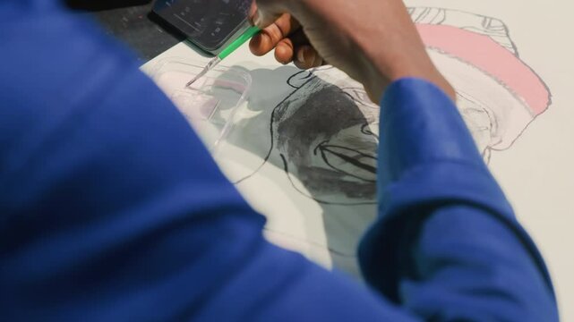 Black artist sketching portrait painting in studio, focused hands using green pencil to shade smiling black man on white paper, smartphone nearby, detailed graphite lines, warm lamp lit atmosphere,