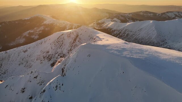 Aerial view of snow-capped mountains under a golden sunset creating a serene landscape with contrasting textures and tones, Nizke Tatry, Zilina Region, Slovakia.