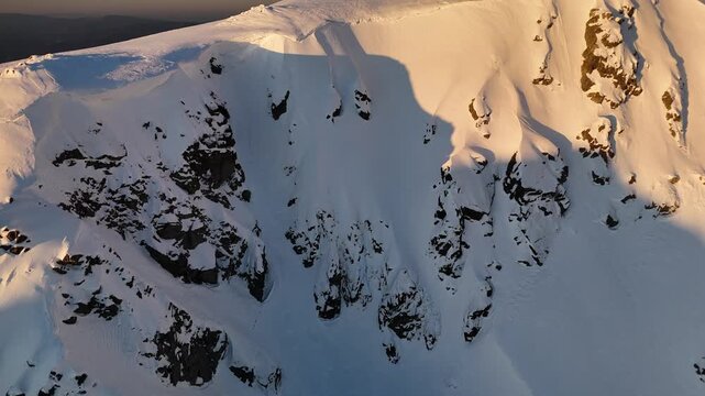 Aerial view of the snow-covered Dumbier mountain, its textured surface reflecting the sunlight, creating a stark contrast of light and shadow, Nizke Tatry, Slovakia.