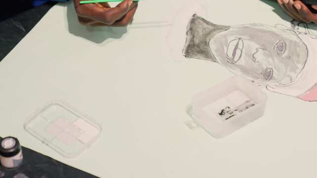 Black man portrait final touches overhead, commercial illustrator refining highlights with green pencil and palette, tabletop tools and ink bottle visible, polished modern studio vibe ready