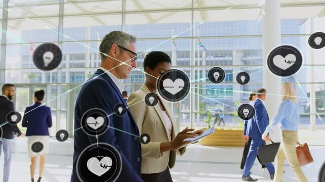 Heart and lightbulb icons connecting with lines over multiracial coworkers discussing in corridor