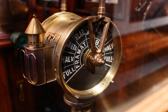 Vintage brass ship's engine order telegraph. A close-up of a vintage maritime engine order telegraph made of polished brass, featuring a black dial with commands in swedish.