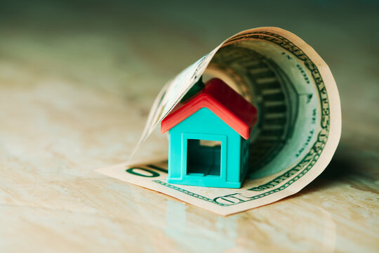 a toy house enclosed by a rolled dollar bill
