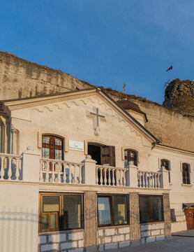 White Christian church of Panteleimon Healer of Inkerman Monastery with large cross, balcony and brown windows, built into rocky cliff under clear blue sky. Sevastopol, Crimea - October 9, 2014