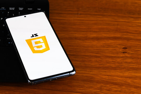Punta Arenas, Chile &ndash; March 31, 2026: The JavaScript (JS) shield logo displayed on a smartphone screen resting on a wooden desk next to a laptop