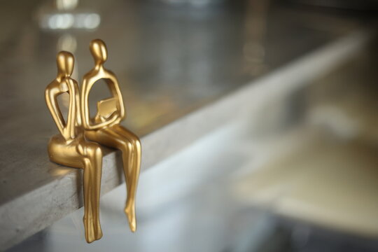 Modern golden abstract thinker statues sitting on a marble ledge, symbolic minimalist figures representing contemplation, philosophy, and home decor.