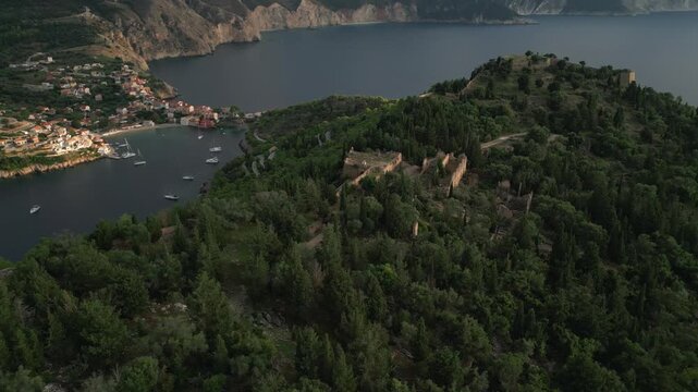 View of a coastal village nestled in a bay, with lush green hills and ancient ruins dotting the landscape.