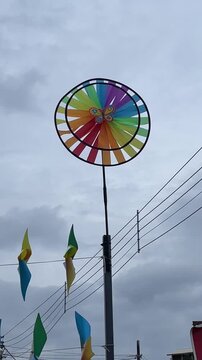 A vertical view of a large colorful rainbow windmill spinning against a cloudy sky at Titi Village landmark in Negeri Sembilan Malaysia.