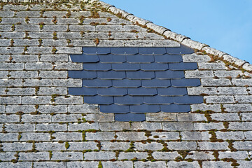 Old stone roof with patch of new black slate tiles and moss growth © Holger