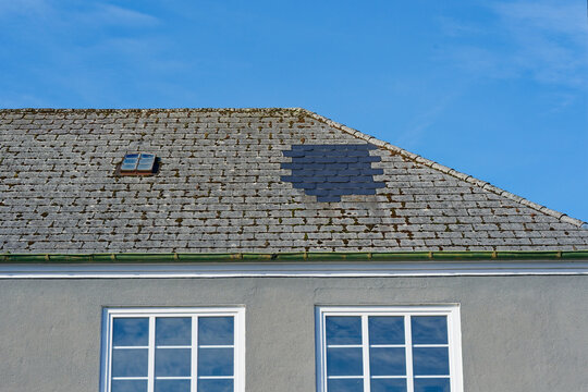 Old house roof with Repaired roof new black tiles and two white framed windows under blue sky
