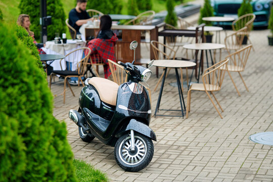 Minsk, Belarus. Jun 27, 2025. MINSK Vesna 125 stylish city scooter parked near outdoor cafe terrace with people dining, relaxing in urban lifestyle setting. Parked moped in front of restaurant terrace