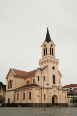Fototapeta premium Church building with tower located in Zrenjanin, Serbia under cloudy sky. Religious architecture and European city landmark.