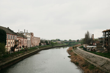 Fototapeta premium Wide view of river with embankment path and buildings in Zrenjanin, Serbia. Urban landscape and European travel concept.