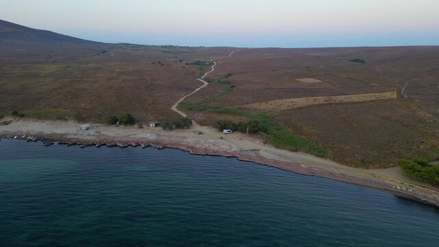 Aerial view of Paralia Skidi beach on Limnos Island, Greece, featuring a parked campervan beside a remote coastline. Clear Mediterranean water and rugged terrain highlight peaceful wild camping