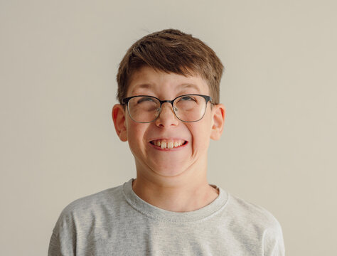 Boy with glasses making funny face smiling tightly against neutral background playful expression concept