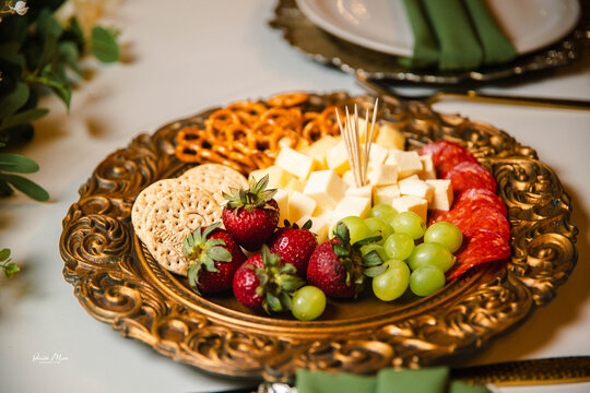 Gourmet charcuterie arrangement served on an elegant gold metal tray with fruits, cheese, and artisanal snacks.