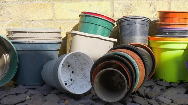 Closeup dolly shot of empty plastic nursery grow plant pots of various colors and sizes, stacked outside against a brick wall in a garden or yard.