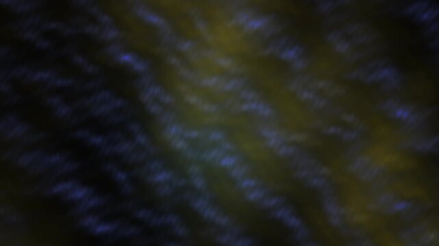Blurry abstract background with blue and yellow hues in a dark setting with a shallow depth of field.