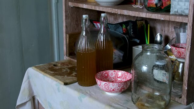 Series shows a woman preparing kombucha in a rural Ukrainian home. She rinses the tea mushroom, cleans jars, pours fermented drink into bottles, highlighting traditional lifestyle and health benefits.