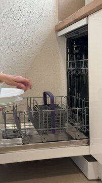 Housewife's hand neatly placing dirty forks and spoons into the silverware basket, pushing the lower rack of the dishwasher back, and closing the door for an automated wash cycle