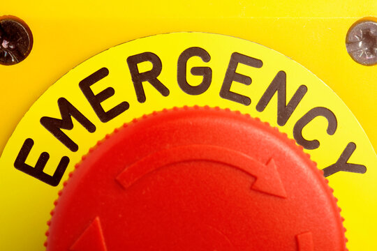 Close up of a red industrial emergency stop button on a yellow background. Macro shot of safety switch for industrial machinery, security protocols, and crisis management concepts.
