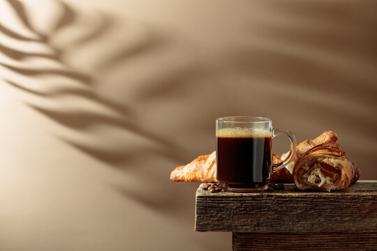 Black coffee with croissants on an old wooden table.