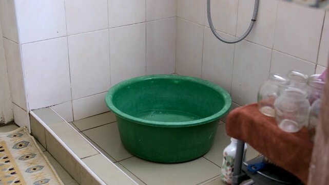 Old green basin standing in a simple rural wash area with sink. Everyday household item used for washing, laundry, or personal hygiene in a traditional village home.