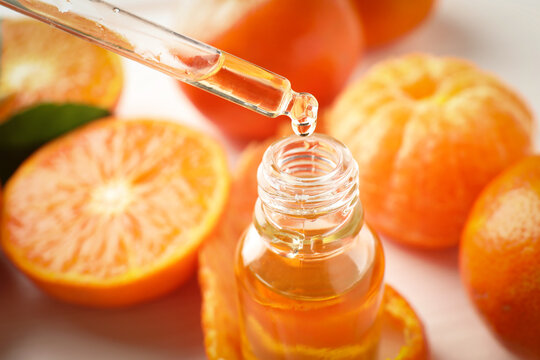 Taking tangerine essential oil from bottle with pipette and fruits on white table, closeup