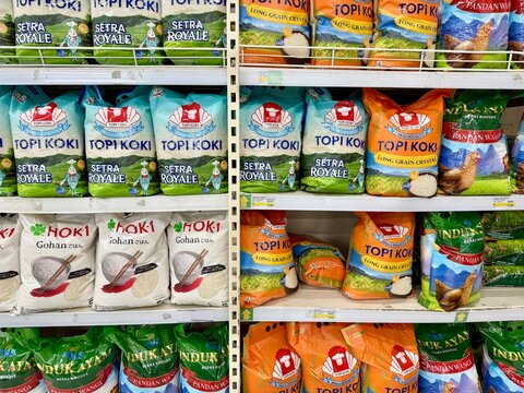 Depok, Indonesia - March 31, 2026: A variety of 5kg rice bags from popular Indonesian brands including Topi Koki, Hoki, and Induk Ayam are stacked on a retail aisle rack at Tip Top Supermarket